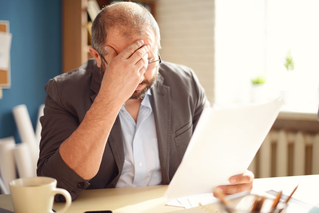 Erbe ausschlagen: Mann sitzt verzweifelt vor dem Papierkram.