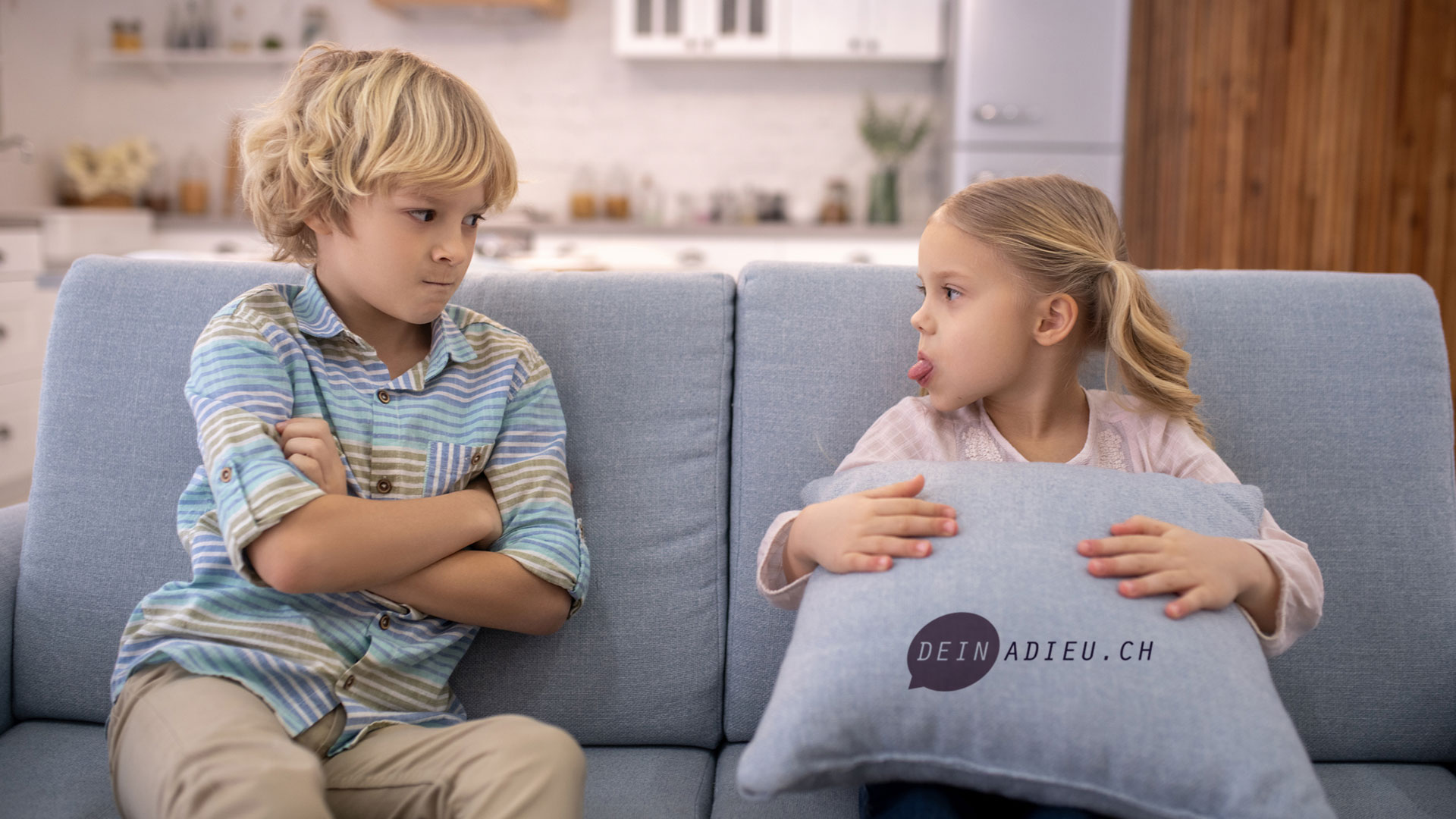 zwei Geschwister sitzen auf dem Sofa und schenken sich böse Blicke.